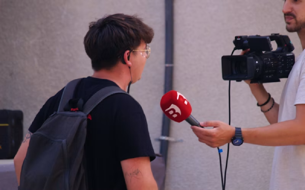 Un giornalista intervista un ragazzo in strada con microfono e videocamera